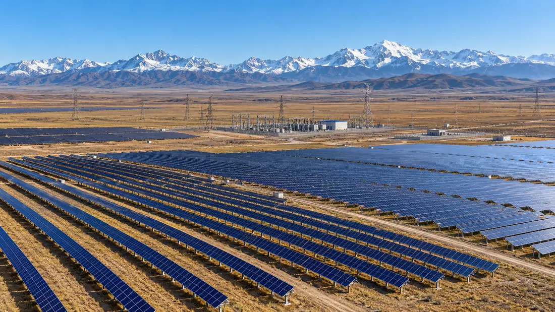 Utility-scale solar project on a Central Asian plain beneath snow-capped mountains